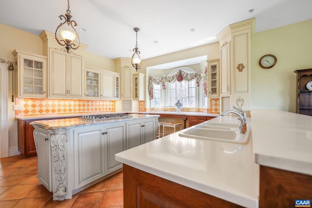 kitchen featuring backsplash, light tile floors, decorative light fixtures, sink, and stainless steel gas stovetop