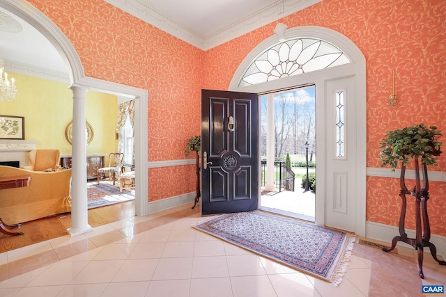 tiled entryway featuring a notable chandelier, crown molding, and decorative columns