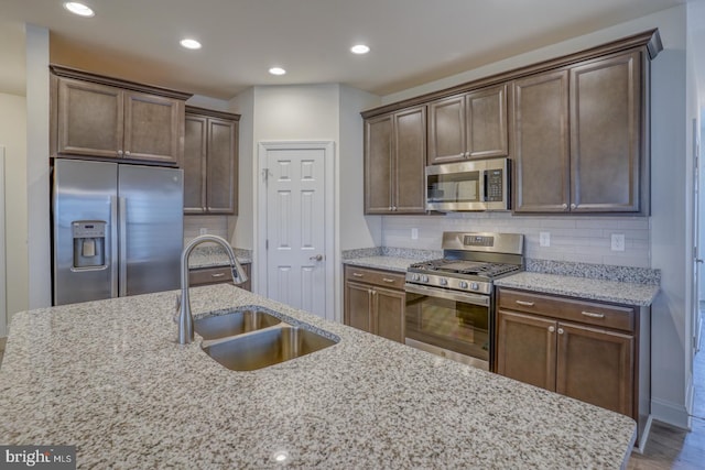 kitchen featuring tasteful backsplash, stainless steel appliances, sink, and light stone counters