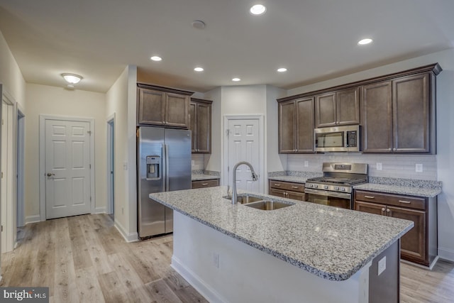 kitchen featuring light stone countertops, appliances with stainless steel finishes, sink, light hardwood / wood-style flooring, and tasteful backsplash