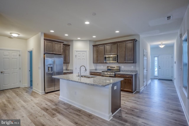 kitchen with appliances with stainless steel finishes, light hardwood / wood-style floors, sink, a center island with sink, and light stone counters