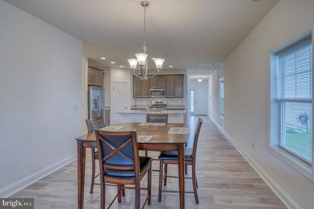 dining area featuring sink, a notable chandelier, light hardwood / wood-style floors, and a healthy amount of sunlight