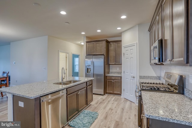 kitchen with appliances with stainless steel finishes, light hardwood / wood-style floors, tasteful backsplash, a kitchen island with sink, and sink