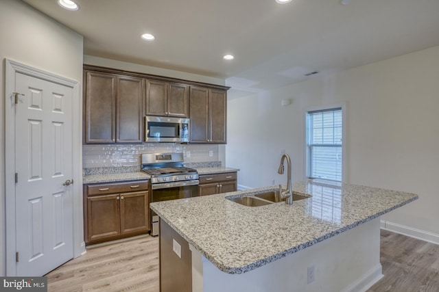 kitchen with light stone counters, tasteful backsplash, stainless steel appliances, light hardwood / wood-style flooring, and sink