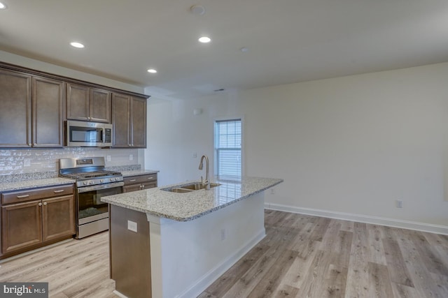 kitchen with light stone countertops, sink, light hardwood / wood-style flooring, stainless steel appliances, and a center island with sink