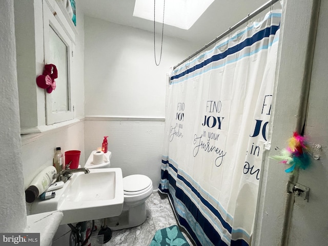 bathroom featuring a skylight, sink, toilet, and tile floors