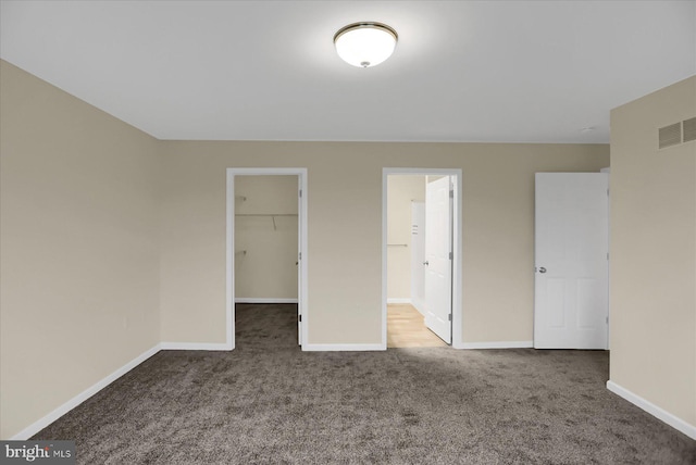 unfurnished bedroom with a spacious closet, a closet, and carpet flooring