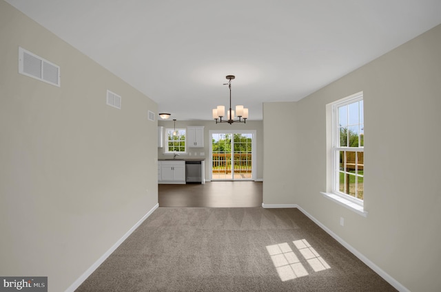 unfurnished dining area with dark colored carpet, plenty of natural light, and a chandelier