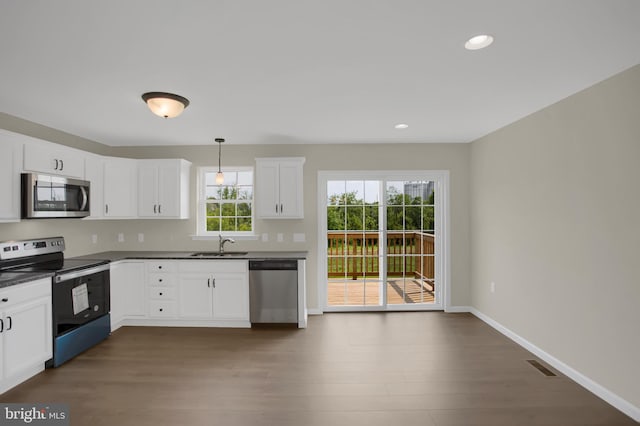 kitchen with appliances with stainless steel finishes, sink, white cabinets, dark hardwood / wood-style flooring, and hanging light fixtures