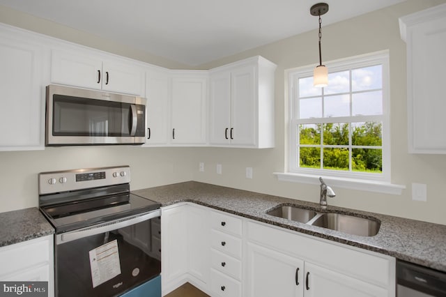 kitchen featuring sink, dark stone countertops, white cabinets, hanging light fixtures, and stainless steel appliances