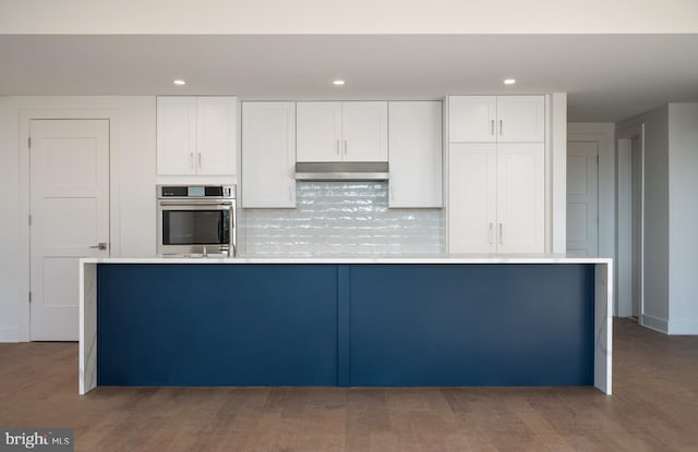 kitchen featuring white cabinets, backsplash, stainless steel oven, and hardwood / wood-style flooring