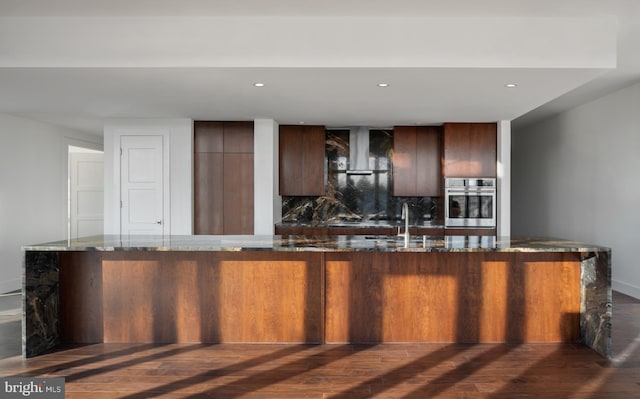 kitchen featuring oven, dark stone counters, backsplash, and dark wood-type flooring