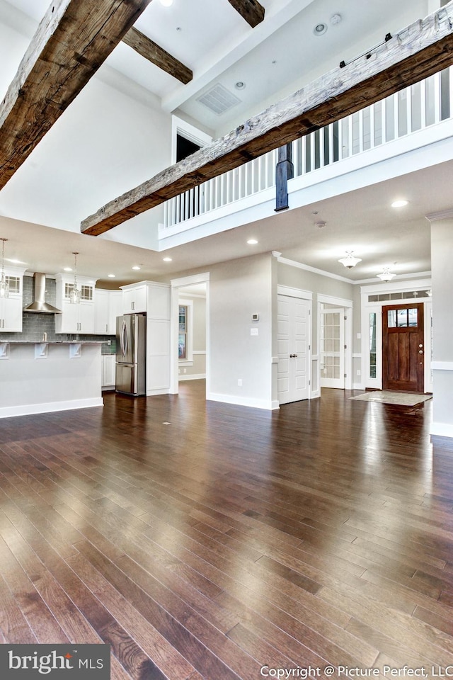 unfurnished living room featuring beam ceiling, dark hardwood / wood-style flooring, and a high ceiling