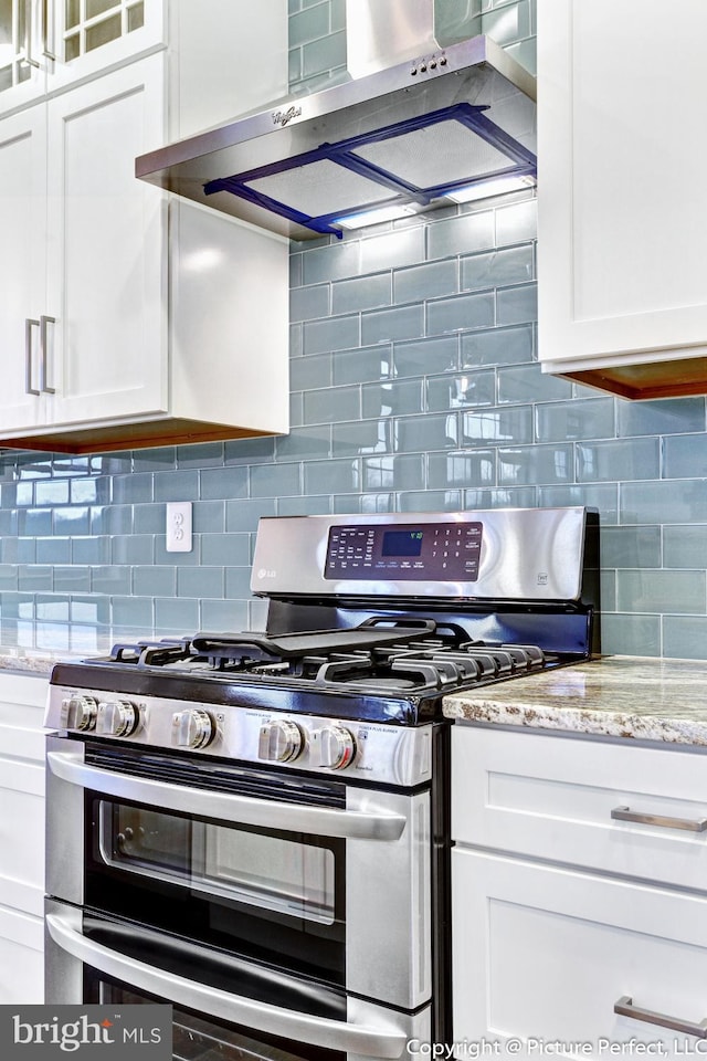 kitchen with light stone countertops, range with two ovens, white cabinets, tasteful backsplash, and wall chimney exhaust hood