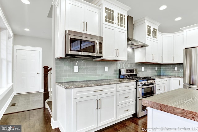 kitchen featuring wall chimney range hood, stainless steel appliances, backsplash, white cabinetry, and dark hardwood / wood-style floors