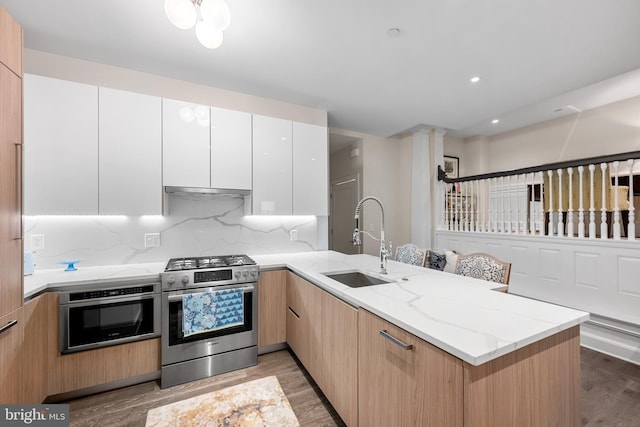 kitchen with stainless steel appliances, wood-type flooring, white cabinetry, light stone counters, and sink