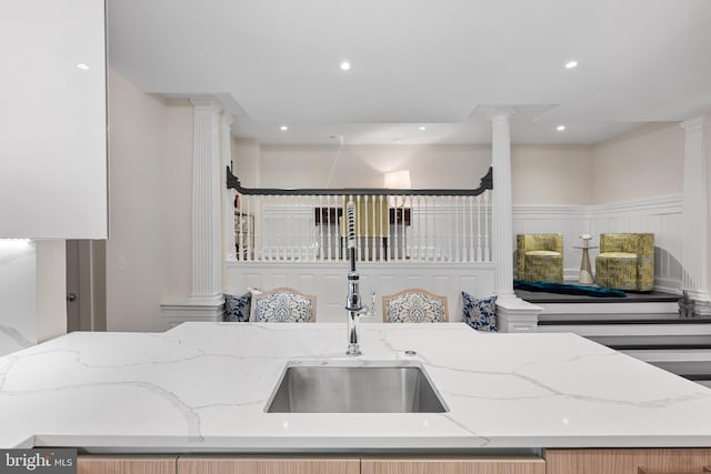 kitchen featuring ornate columns, light stone counters, and sink