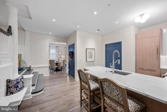 kitchen with a kitchen breakfast bar, light stone counters, hardwood / wood-style floors, decorative columns, and sink