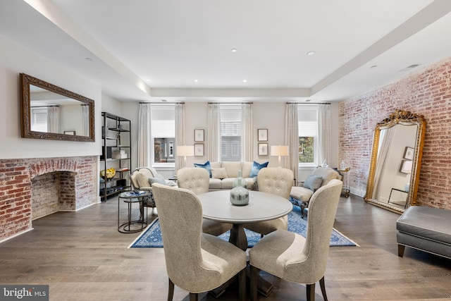 dining room with brick wall, dark hardwood / wood-style flooring, a fireplace, and a tray ceiling