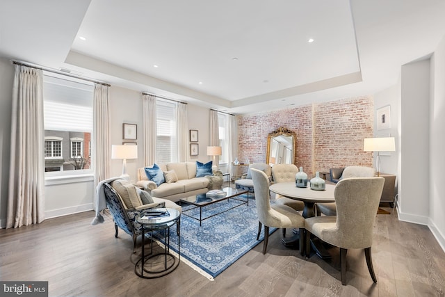 living room with brick wall, wood-type flooring, and a tray ceiling