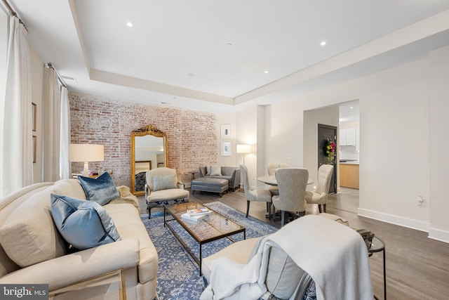 living room featuring a raised ceiling, brick wall, and dark wood-type flooring