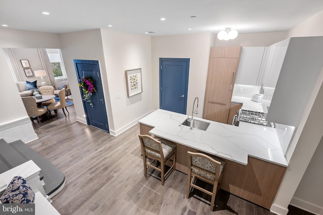 kitchen with kitchen peninsula, sink, light stone counters, a kitchen breakfast bar, and light hardwood / wood-style floors