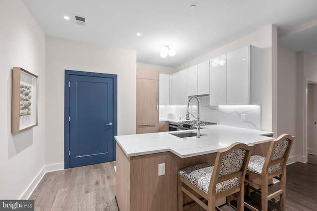 kitchen featuring tasteful backsplash, light stone counters, a breakfast bar, light hardwood / wood-style flooring, and white cabinets