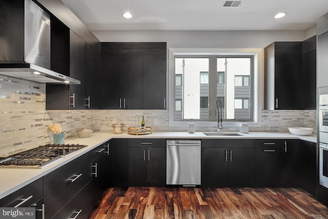 kitchen featuring sink, dark hardwood / wood-style flooring, appliances with stainless steel finishes, wall chimney range hood, and tasteful backsplash