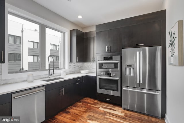 kitchen with appliances with stainless steel finishes, sink, backsplash, and hardwood / wood-style flooring