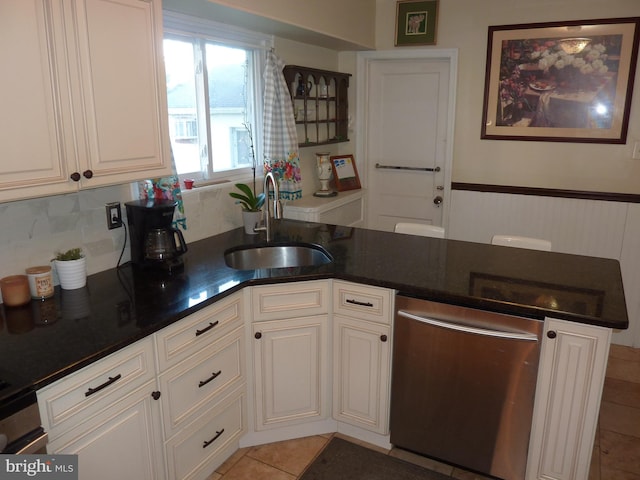 kitchen with sink, light tile floors, white cabinets, dark stone counters, and stainless steel dishwasher