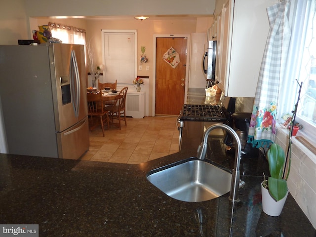 kitchen featuring dark stone countertops, appliances with stainless steel finishes, sink, and light tile floors