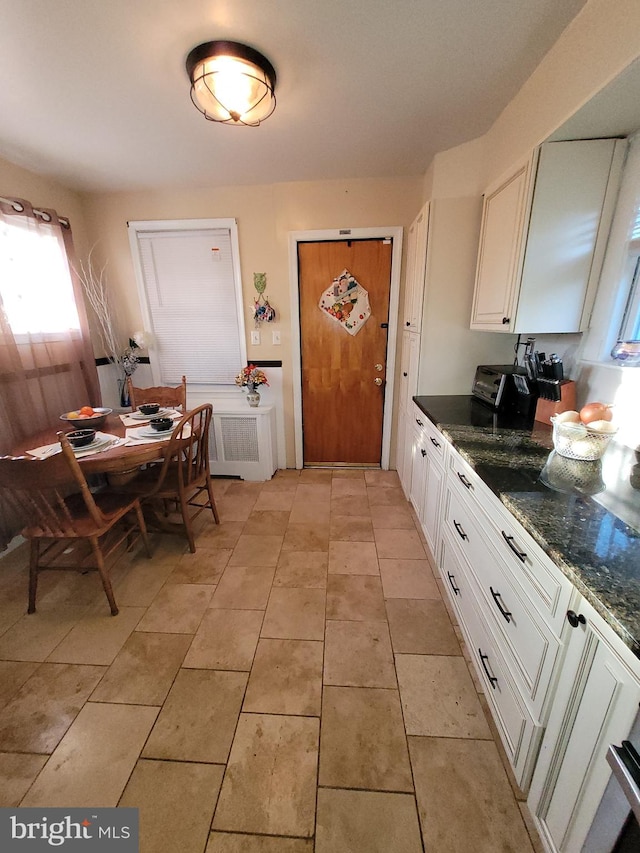 kitchen with light tile flooring, radiator heating unit, dark stone countertops, and white cabinets