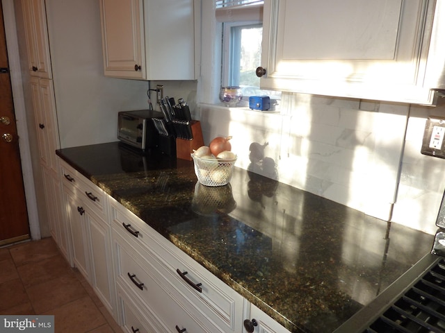 kitchen with tile floors, dark stone countertops, and white cabinets