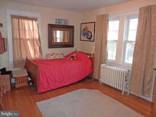 bedroom featuring dark wood-type flooring, multiple windows, and radiator heating unit