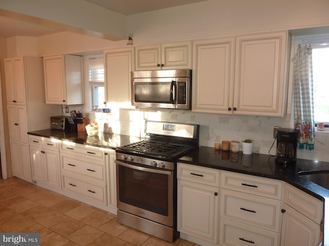 kitchen featuring appliances with stainless steel finishes, white cabinetry, light tile floors, and a healthy amount of sunlight