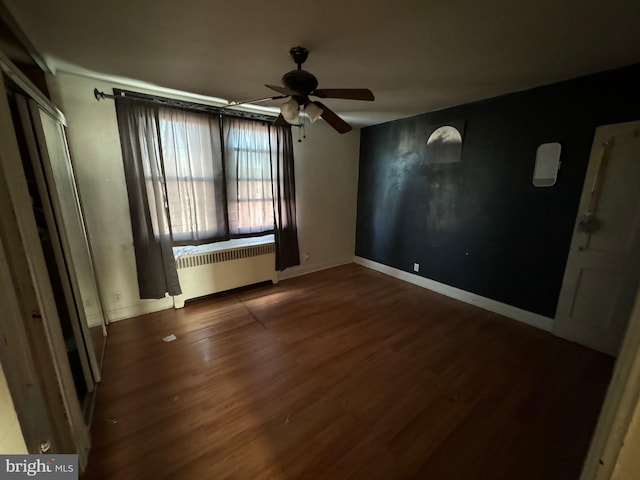 empty room featuring ceiling fan, dark wood-type flooring, and radiator heating unit