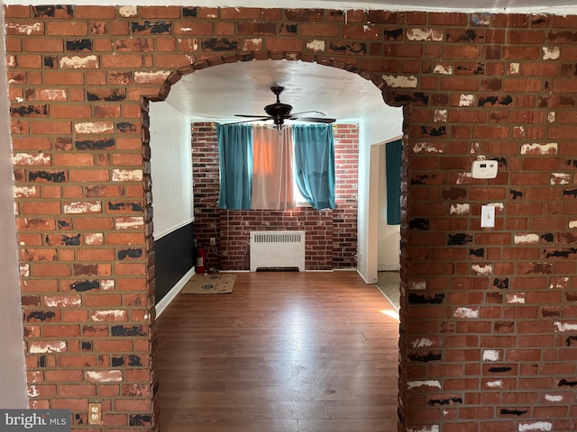 interior space with radiator heating unit, dark wood-type flooring, ceiling fan, and brick wall