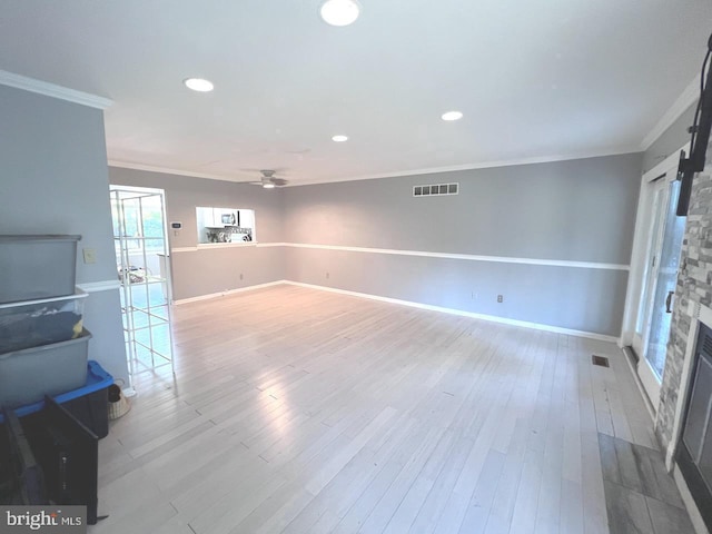 living room with hardwood / wood-style floors, a stone fireplace, ceiling fan, and crown molding