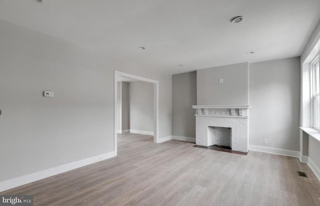 unfurnished living room featuring a brick fireplace and light wood-type flooring