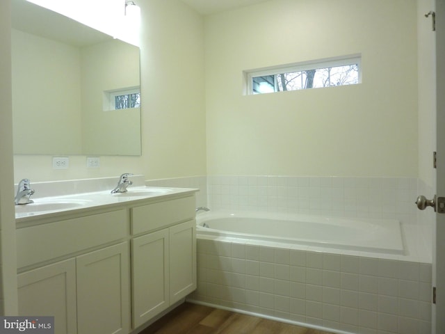 bathroom featuring tiled bath, hardwood / wood-style flooring, and dual bowl vanity