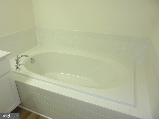 bathroom with hardwood / wood-style flooring, vanity, and tiled tub