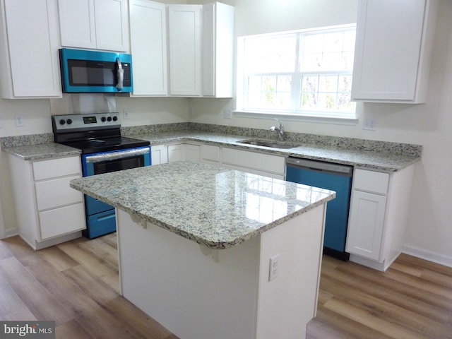 kitchen featuring appliances with stainless steel finishes, white cabinetry, light hardwood / wood-style flooring, a center island, and sink