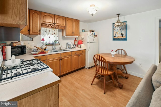 kitchen with decorative light fixtures, white fridge, sink, and light wood-type flooring