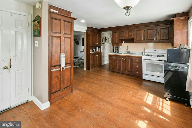 kitchen with dishwasher, gas range gas stove, tasteful backsplash, sink, and dark hardwood / wood-style flooring