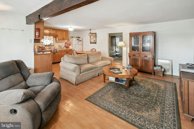 living room with sink, beam ceiling, and light wood-type flooring