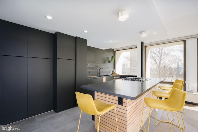 interior space with a kitchen bar, tile flooring, gray cabinetry, backsplash, and sink