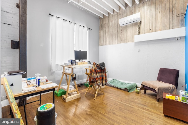 home office with light hardwood / wood-style flooring, beamed ceiling, and a wall unit AC