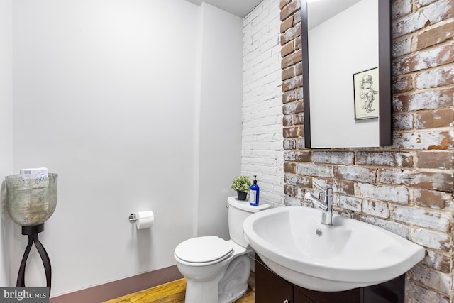 bathroom with vanity with extensive cabinet space, brick wall, toilet, and wood-type flooring