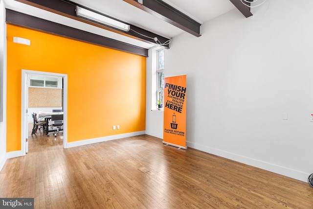 unfurnished room with light wood-type flooring, a wealth of natural light, and beamed ceiling