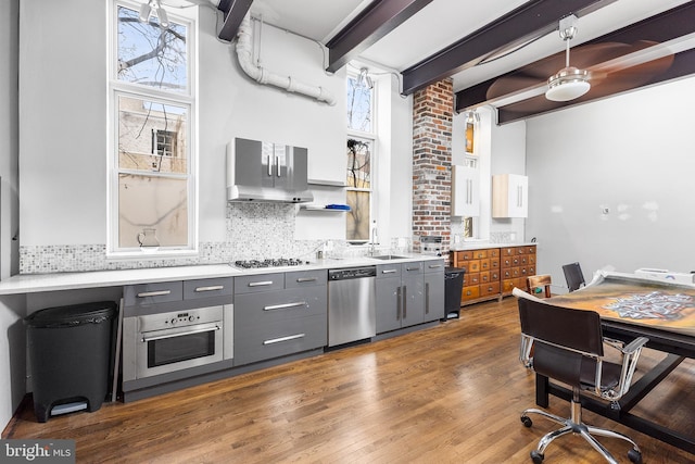 kitchen with beamed ceiling, gray cabinets, dark wood-type flooring, appliances with stainless steel finishes, and backsplash